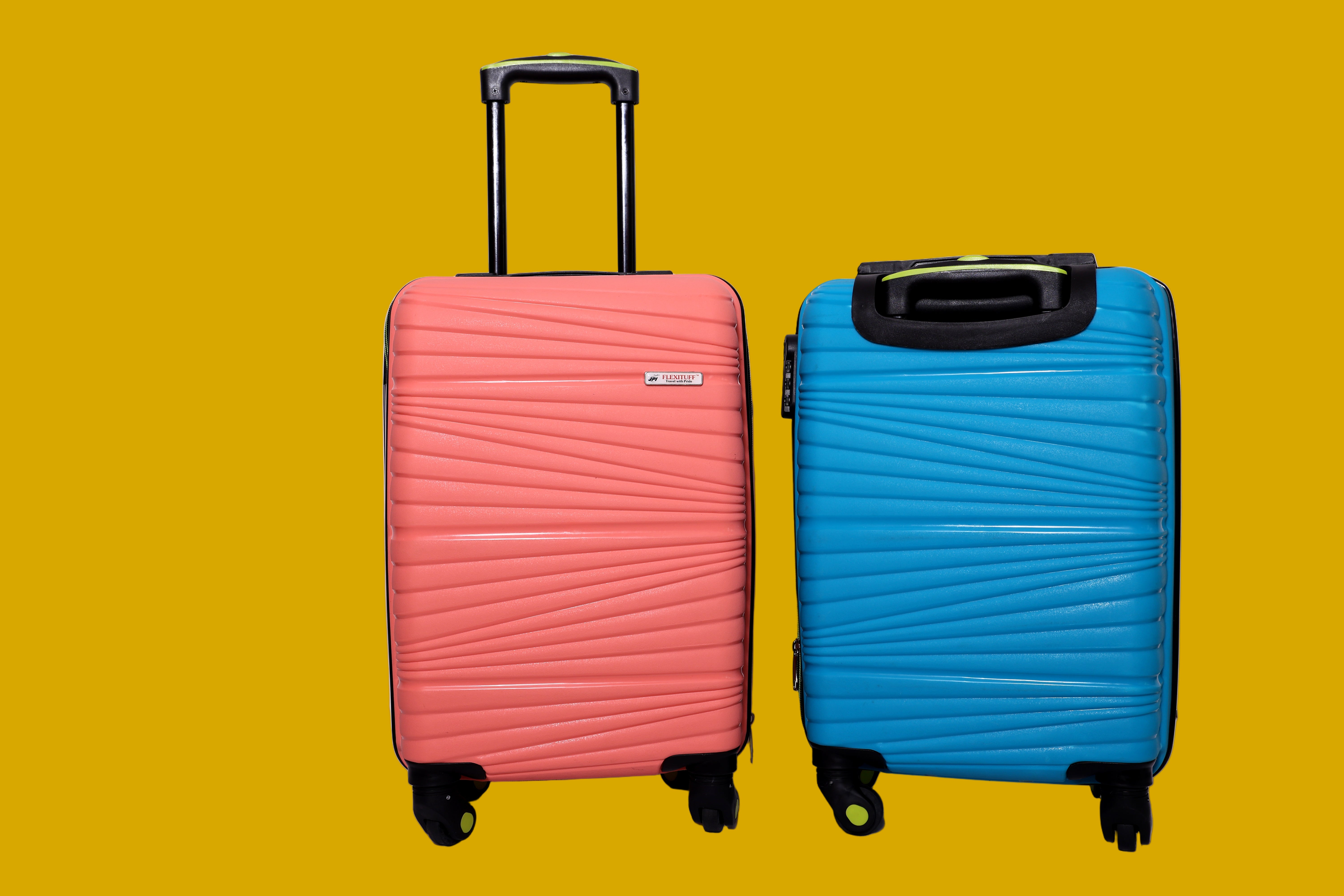Two suitcases with trolley, one pink and one blue, on a mustard background.